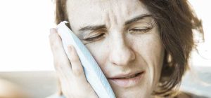 Woman holding a cloth to her cheek with a pained expression, suggesting tooth pain