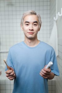 Young man holding a toothbrush and toothpaste in a tiled bathroom