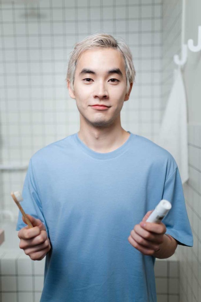 Young man holding a toothbrush and toothpaste in a tiled bathroom