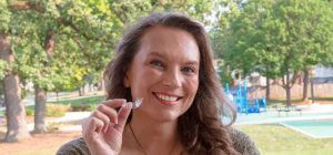 Smiling woman holding a clear aligner tray outdoors
