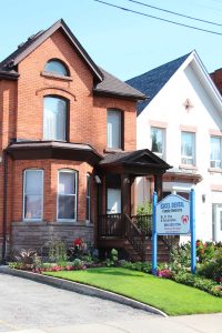 Front exterior of Excel Dental office in Hamilton, Ontario, with building entrance and roadside sign.