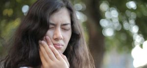 Young woman holding her cheek as if experiencing tooth or jaw pain