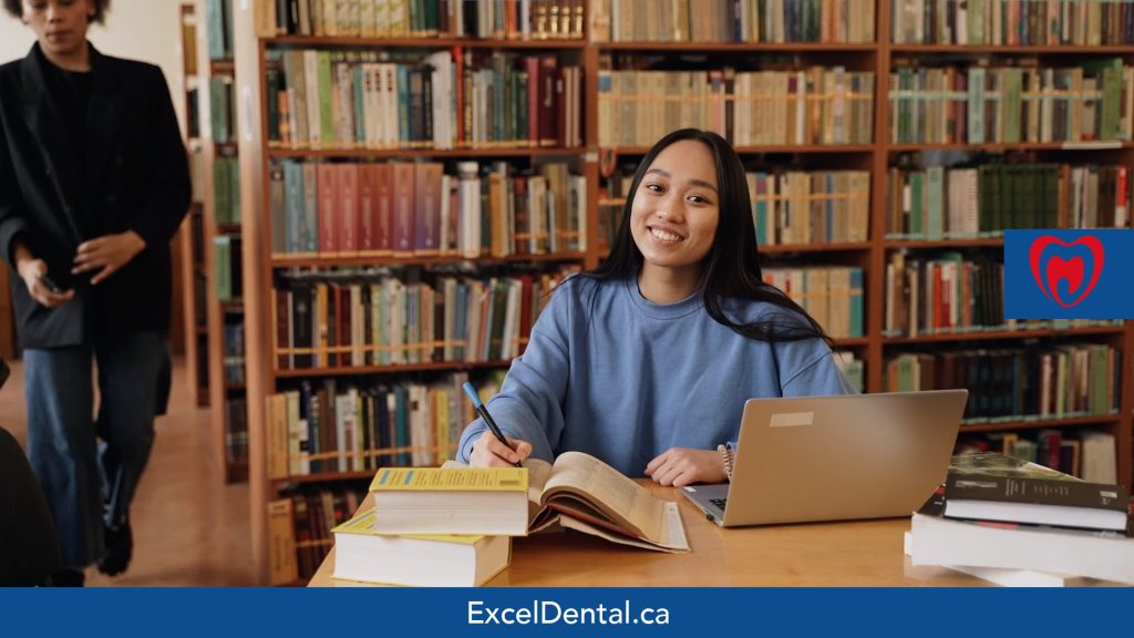 Smiling young woman studying at a table with books and a laptop in a library
