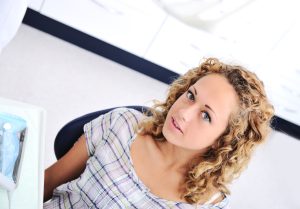 Woman seated in a dental chair in a bright dental office, looking upward.