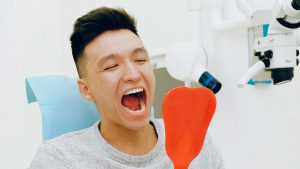 Smiling man in a dental chair holding a hand mirror with his mouth open