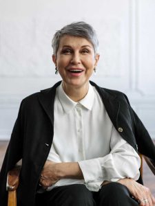 Older woman with short gray hair smiling while seated in a chair