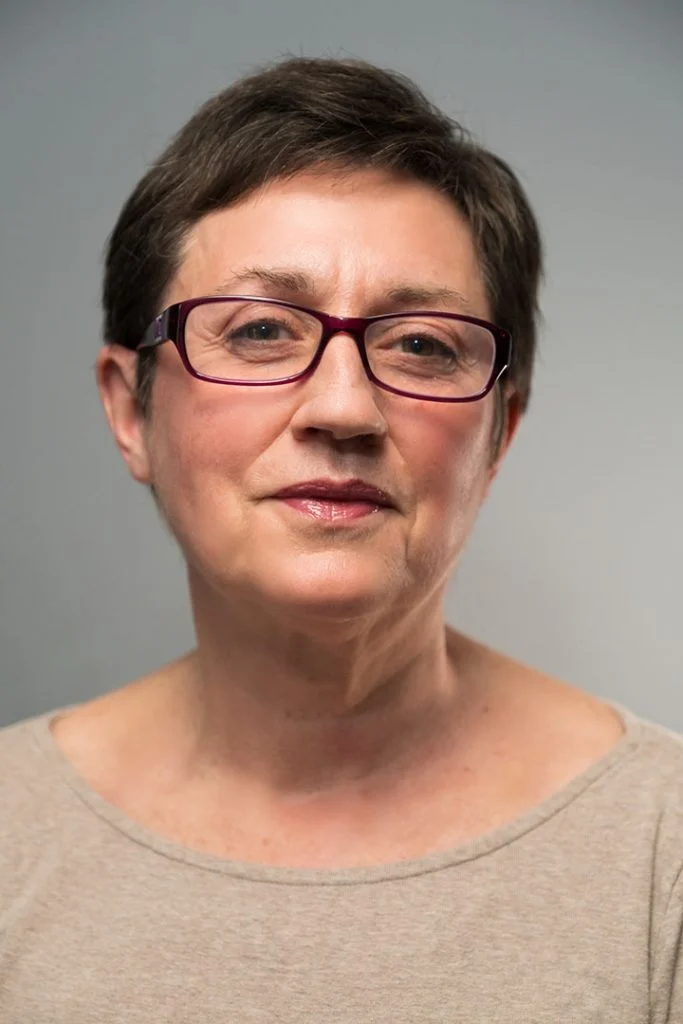 Head-and-shoulders portrait of a woman with short hair and glasses against a gray background.