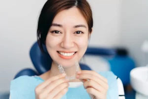 Smiling young woman in a dental chair holding a clear aligner tray.