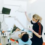 Dental professional adjusts exam light while a patient reclines in a treatment chair