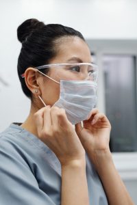 Woman in scrubs wearing protective goggles and adjusting a face mask