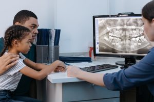 Dentist showing a child patient and accompanying adult a dental X-ray during a consultation