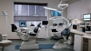 Modern dental treatment room with two chairs, monitors, and overhead lights