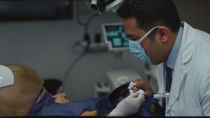 Dentist wearing a mask examines a patient in a dental chair during a treatment appointment.