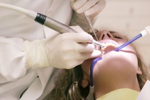 Dentist treating a patient’s teeth with a handpiece, mirror, and suction tube