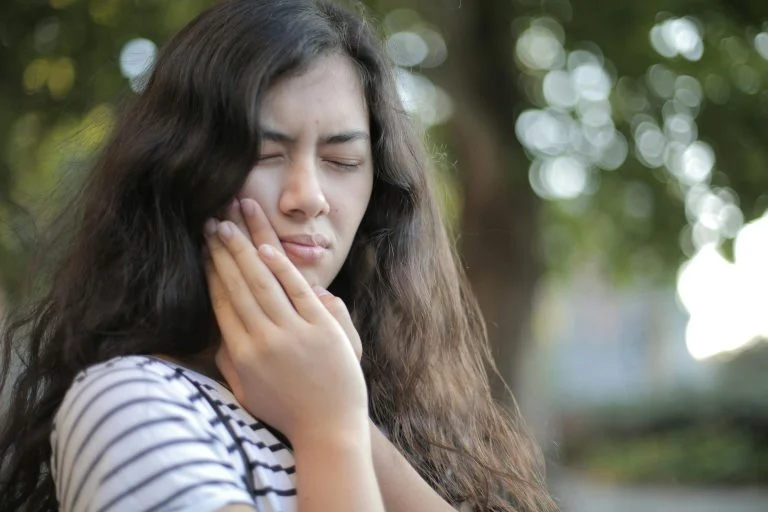 Woman outdoors holding her cheek as if experiencing tooth pain