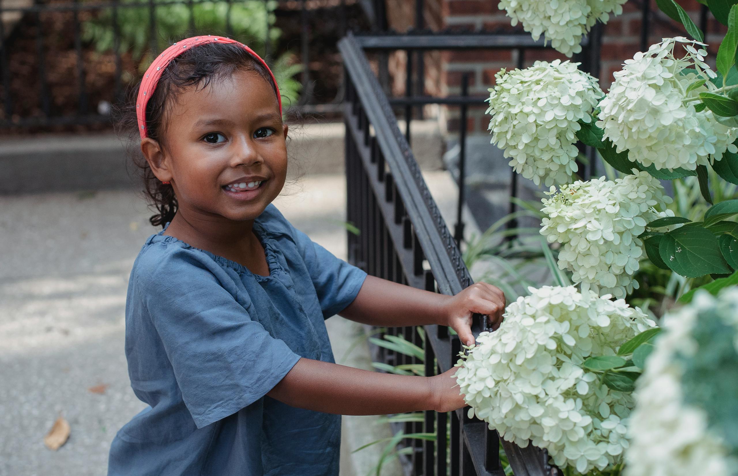 Smiling child beside white hydrangea flowers in a garden.