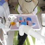 Dental operatory with a patient in the chair, clinician nearby, and instruments arranged on a tray.