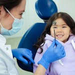 Dentist showing a dental mirror to a smiling child seated in a dental chair.