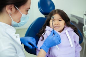 Dentist showing a dental mirror to a smiling child seated in a dental chair.