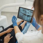 Dentist showing a dental x-ray on a tablet to a patient in a dental chair.