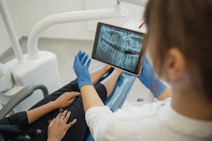 Dentist showing a dental x-ray on a tablet to a patient in a dental chair.