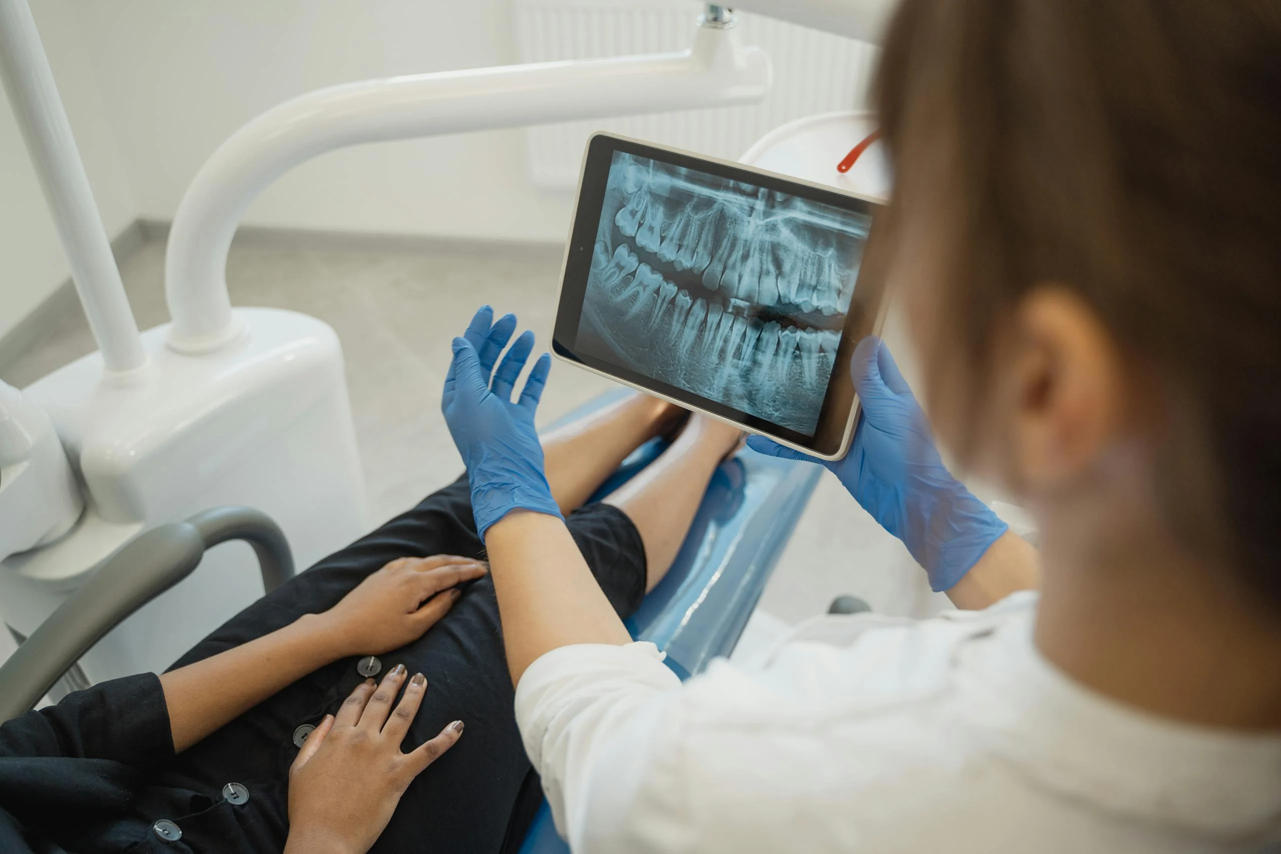 Dentist showing a dental x-ray on a tablet to a patient in a dental chair.