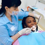 Dentist examining a patient’s teeth during a dental appointment while the patient holds a hand mirror.