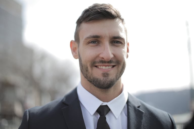 Smiling adult man in a dark suit outdoors with a bright expression.