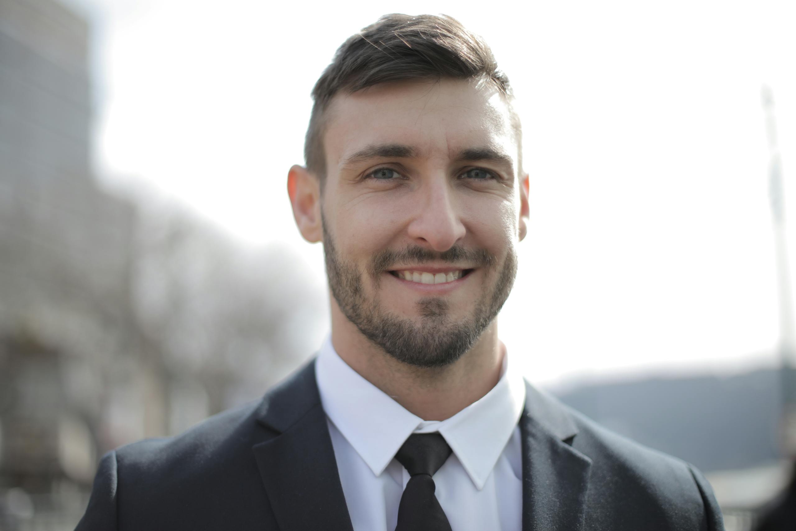 Smiling adult man in a dark suit outdoors with a bright expression.