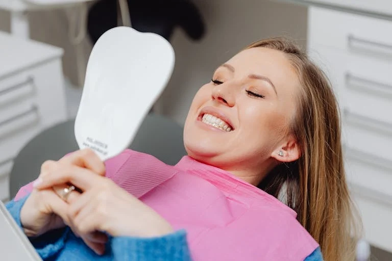 Woman smiling in a dental chair while holding a hand mirror.