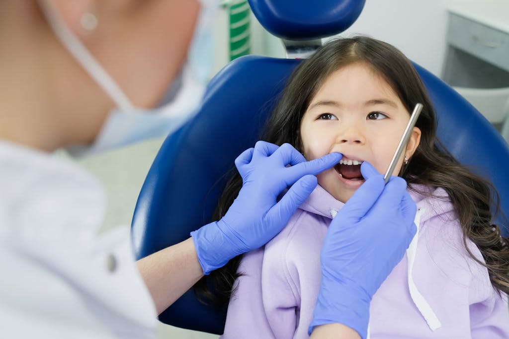Young girl receiving a dental exam in a clinic chair while a dentist uses a mirror.