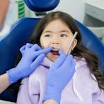 Young girl receiving a dental exam in a clinic chair while a dentist uses a mirror.