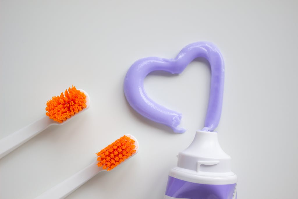Two toothbrushes beside a toothpaste tube with heart-shaped purple toothpaste on a white background.