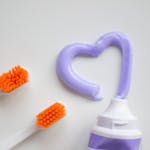 Two toothbrushes beside a toothpaste tube with heart-shaped purple toothpaste on a white background.