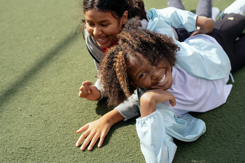 Two smiling girls lying on a sports field outdoors