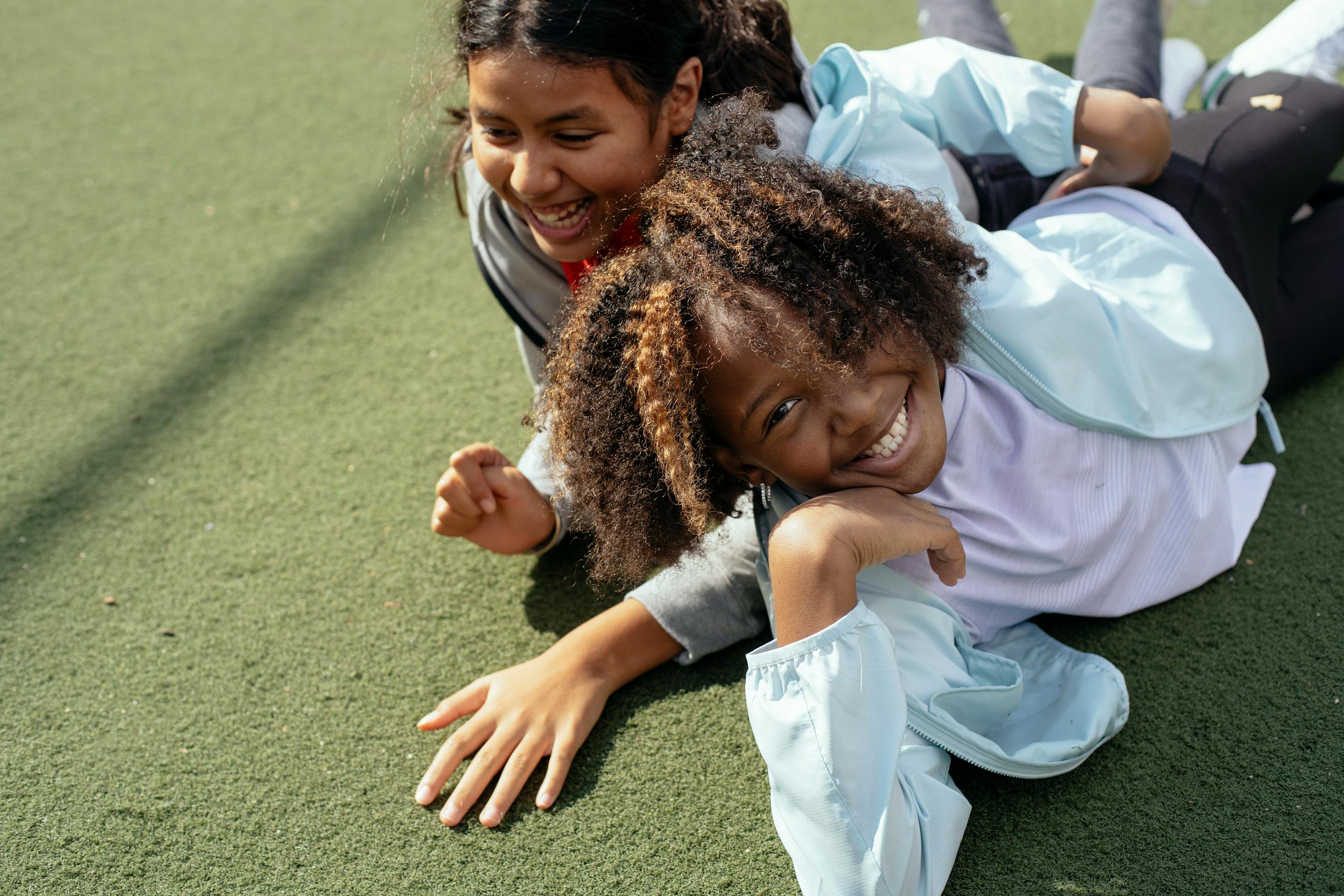 Two smiling girls lying on a sports field outdoors