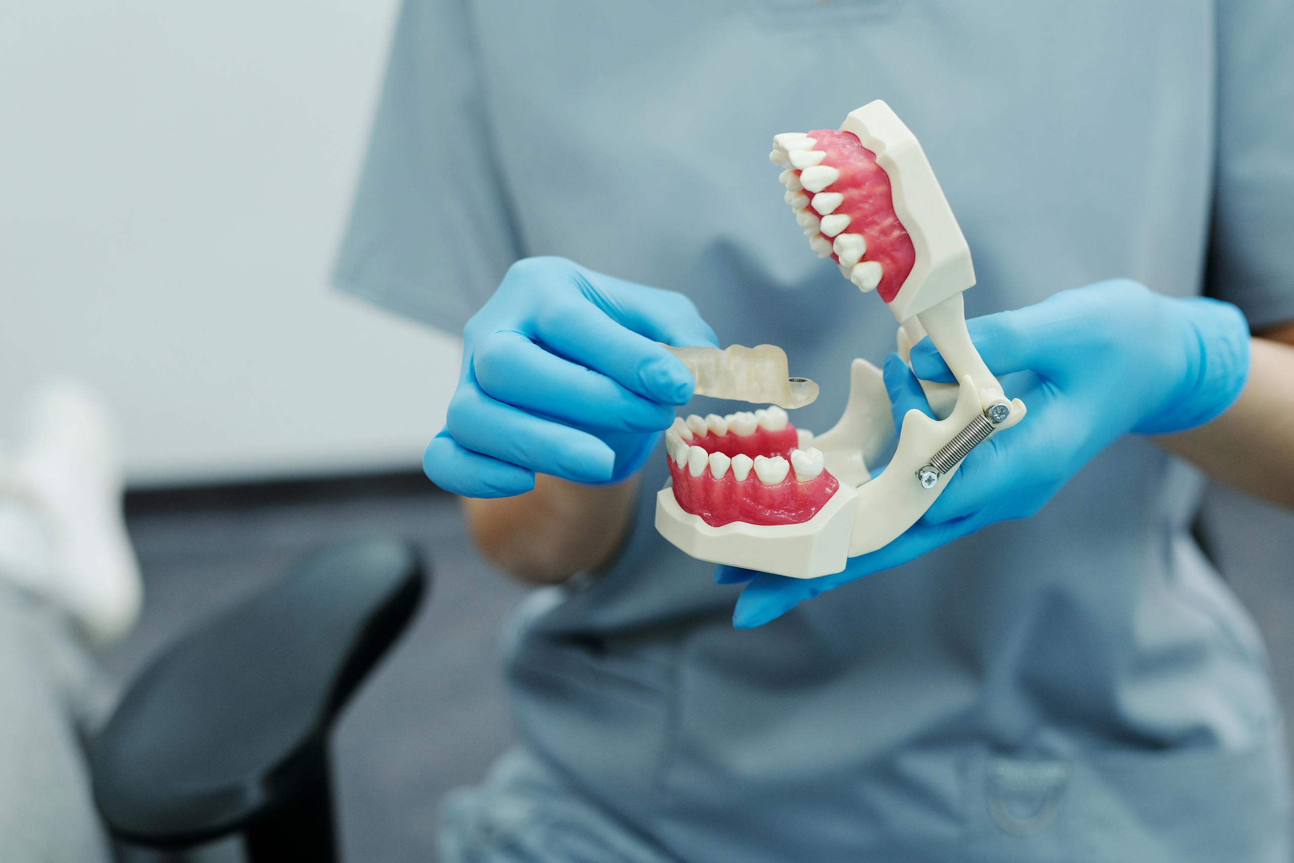 Dental professional holding a teeth model and clear tray during a clinic demonstration.