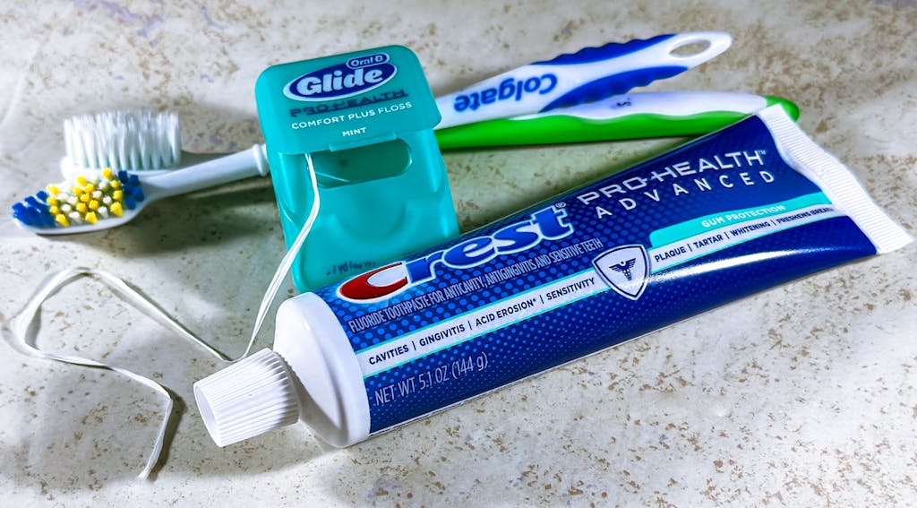 Close-up of toothbrushes, dental floss, and a toothpaste tube on a countertop.