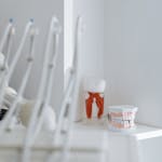 Blurred dental instruments with tooth and denture models on a shelf in a bright clinic.