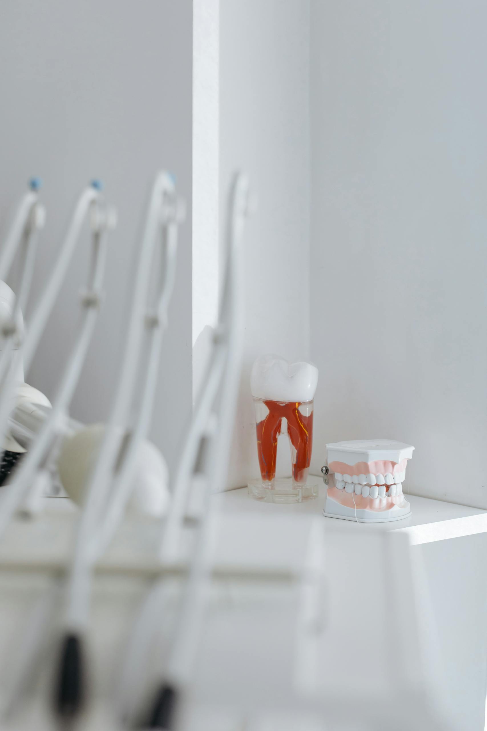 Blurred dental instruments with tooth and denture models on a shelf in a bright clinic.