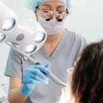 Dentist examining a patient with dental tools and overhead exam light in a modern clinic.