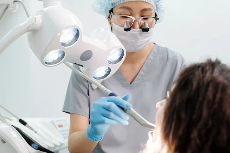 Dentist examining a patient with dental tools and overhead exam light in a modern clinic.