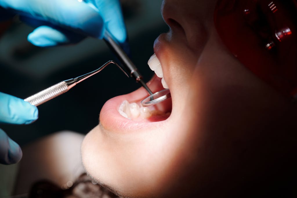 Close-up of a dental exam with a mirror and explorer inspecting a patient's teeth under bright light.