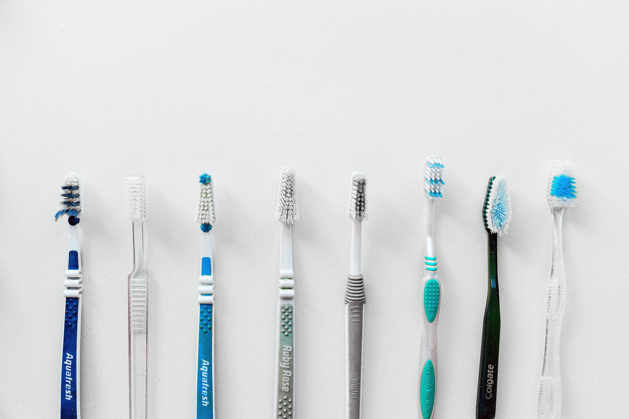 Seven toothbrushes lined up against a white background with copy space above.