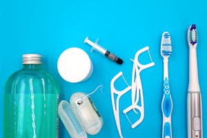 Flat lay of oral hygiene items on a blue surface, including mouthwash, floss picks, a floss container, and toothbrushes.