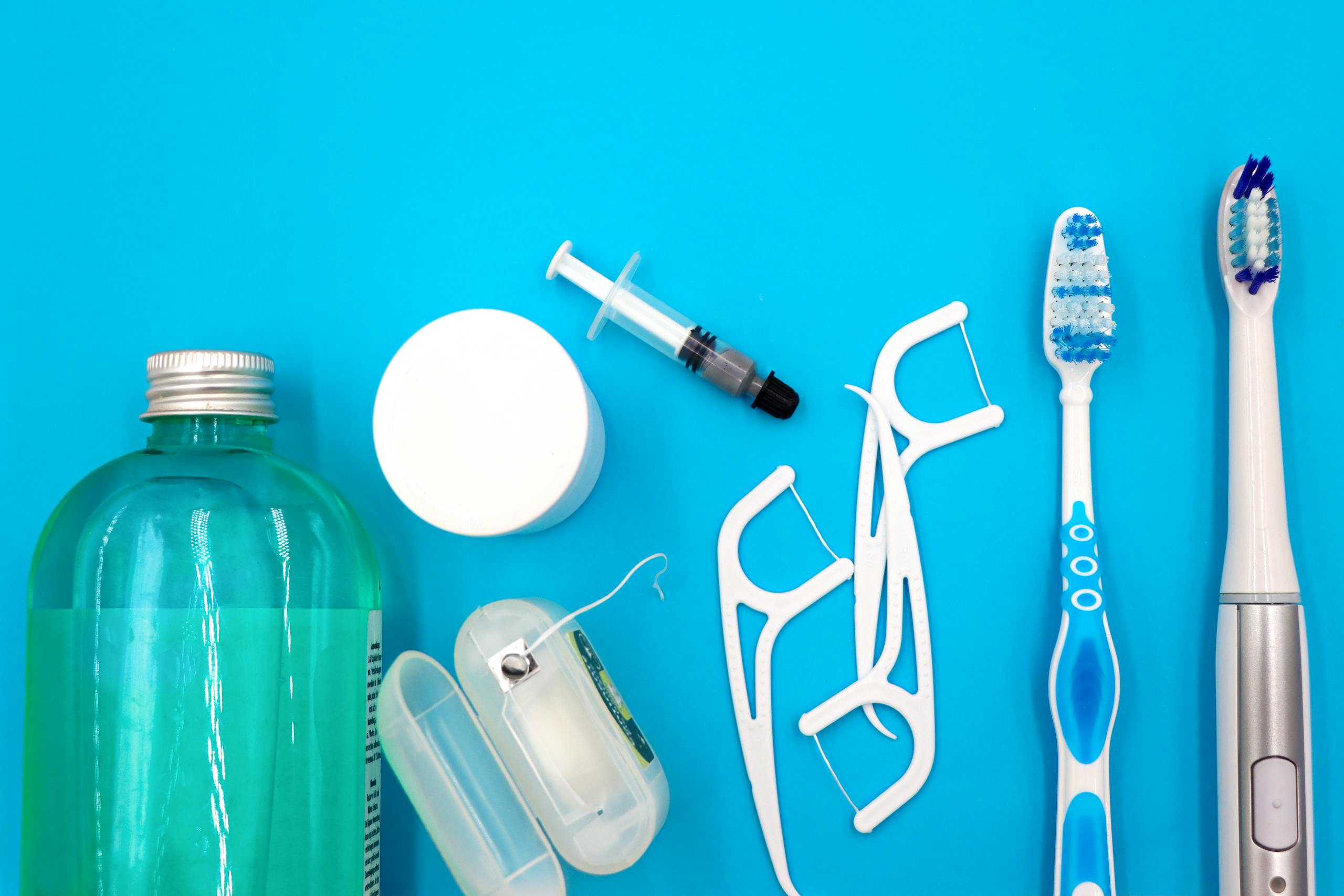 Flat lay of oral hygiene items on a blue surface, including mouthwash, floss picks, a floss container, and toothbrushes.