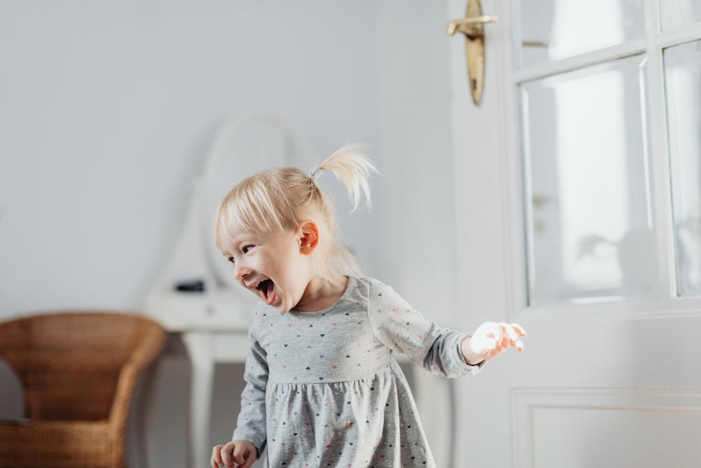Laughing toddler standing in a bright room near a window.
