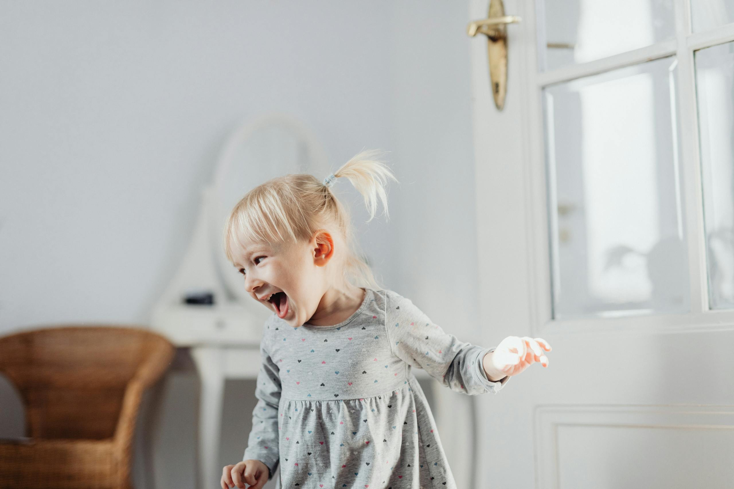Laughing toddler standing in a bright room near a window.