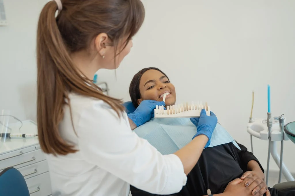Dentist comparing a tooth shade guide with a smiling patient in a dental chair.