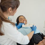 Dentist comparing a tooth shade guide with a smiling patient in a dental chair.